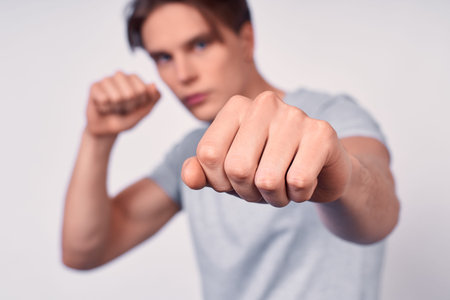 A young aggressive boxer, holding his hands in black boxing gloves near his face, emotion...
