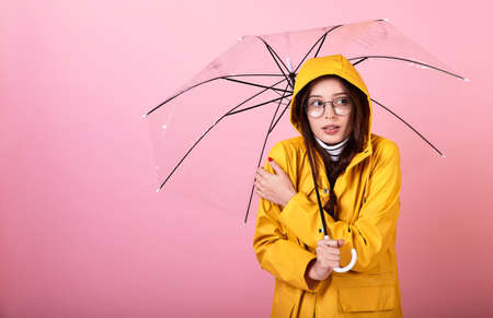 Beautiful Frenchwoman in a gentle blue beret, a striped blouse and a yellow rain jacket with glasses on a pink background. A lady makes a sign with her hands in her heart and shows love. Rainy day.の写真素材