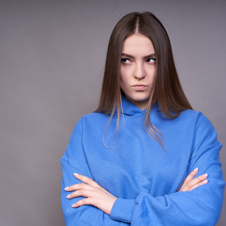 Vertical picture, angry offended young girl, with long healthy hair and brown eyes, crossed her arms...
