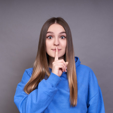 A woman with long blond hair, in a blue hoodie, put her finger to her mouth, asks for silence. A...