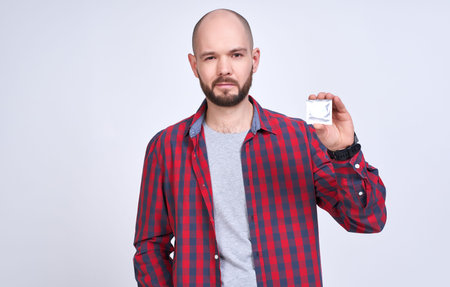 A cute adult man without hair, with brown eyes, in a gray T-shirt and plaid shirt, looks at camera,...