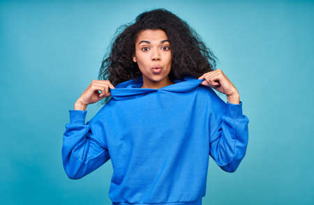 An optimistic teenage girl dressed in a casual blue sweatshirt, smiling happily, standing against a blue background, looking friendly at the camera, standing indoors. Studio portrait.の写真素材