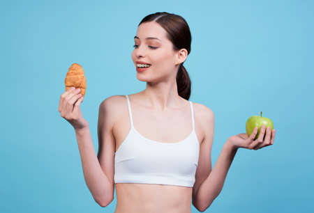 Image of an attractive brown-haired woman with an apple and a croissant.の写真素材