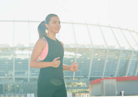 A young, fresh, beautiful, slender girl, wears long dark hair, wears a black sports shirt, enjoys drinking water from a bottle after playing sports, against the backdrop of the city.の写真素材