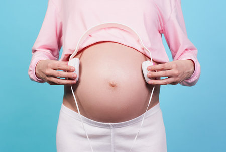 Close-up, belly of a pregnant white girl, at a later date, wears a pink sweater, holds white...