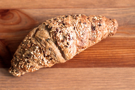 Baked yeast bread croissant with black and white sesame grains, wood background. Blurred background....