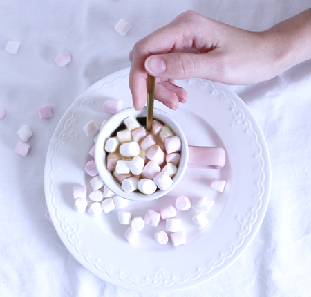 Valentines composition. Womans hand and cup of hot chocolate with Marshmallows, on white table background. Winter breakfast concept. Flat lay, top view.の写真素材