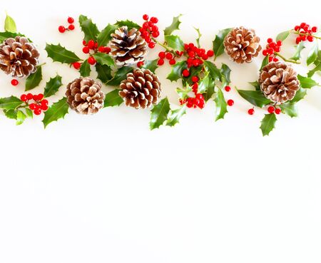 Christmas festive styled floral composition. Pine cones and holly Ilex aquifolium on white table background. Decorative frame, web banner. Flat lay, top view,copy space.の写真素材