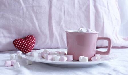 Valentines composition. Cup of hot chocolate with Marshmallows, on the bed. Small red heart on background.Breakfast concept.の写真素材