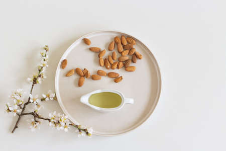 Blooming almond twigs macerating in almond oil, to prepare a skin tonic, earthenware plate and white table background.Spa products concept.の写真素材