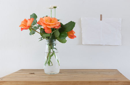 Spring, summer still life scene. Vintage wedding feminine styled photo, floral composition. Empty paper sheets and posters mockups taped on a white wall. Vase with orange roses. Roses concept.の写真素材