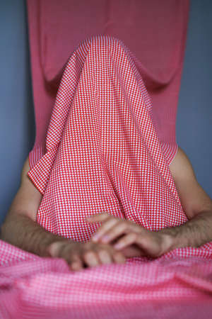 Unrecognisable man covered with colourful cloth sits at the table.の写真素材