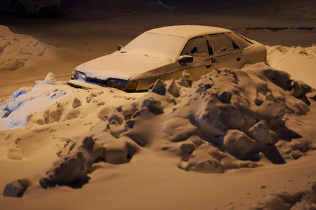 A car littered with snow stands on the side of the night city in the light lamp.の写真素材
