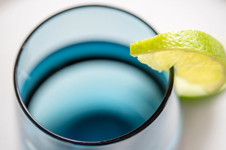 Glass of water with slice of lime, closeup, top view. Water in blue glass with lime macro, white...