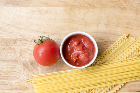 Dry spaghetti, fresh tomato and tomato sauce, top view, room for text. Ingredients of Italian pasta meal, wooden background.の写真素材
