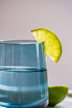 Glass of water with slice of lime, closeup, side view. Water in blue glass with lime, macro, vertical.の写真素材