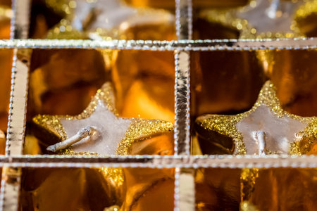 Golden sparkling Christmas ornaments in box, macro. Closeup of festive star shaped candles in gold box.の写真素材