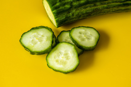 Fresh cucumber and slices, closeup, top view, yellow background.Vibrant healthy cucumber, macro food.の写真素材