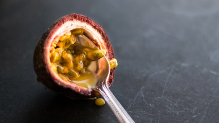 Delicious fresh juicy passionfruit, maracuja half with spoon closeup, dark background.Half mature passionfruit, granadilla, yellow flesh, black seeds.の写真素材