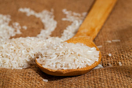 rice grains on a wooden spoon - derevyannnoy spoon scattered grains of rice. Close-up.の写真素材