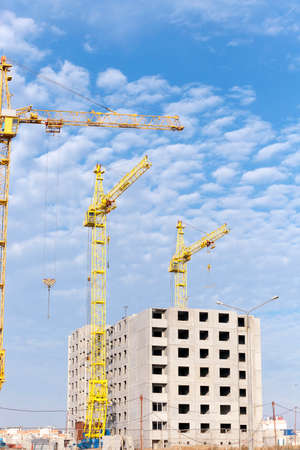 photographed close-up construction cranes during construction of a new multi-storey apartment building, blue sky and clouds,の写真素材