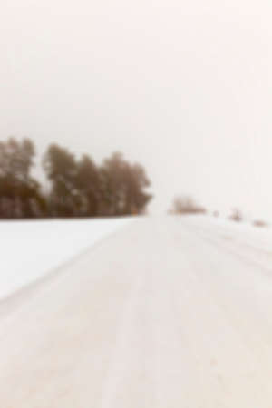 photographed close-up of the road for the movement of vehicles covered with snow, winter season, countryside, empty roadway, sky and trees, defocusedの写真素材