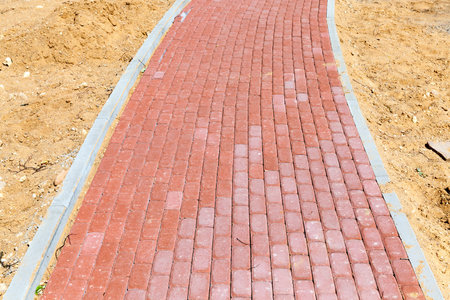 a pedestrian road made of red cobblestones. Sand was poured along the edges of the paving the...