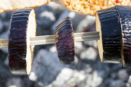few pieces of eggplant while cooking shish kebab on skewers. Photo close-up. Cooking is done in the woods during restの写真素材