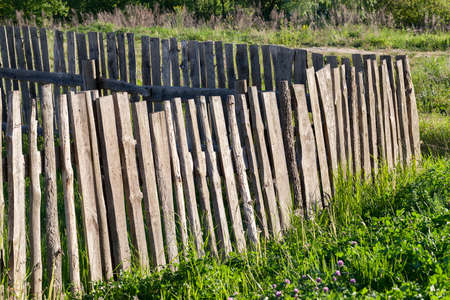an old fence, made of wooden boards, having a lot of defects. Close-up photo of a growing grass near a fenceの写真素材
