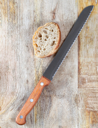 metal knife with a wooden handle and a piece of cut baguette lying together on an old cutting board....