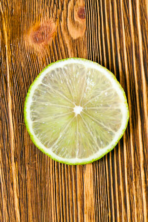 Fresh juicy slice of green lime, photographed close-up on an old wooden table.の写真素材