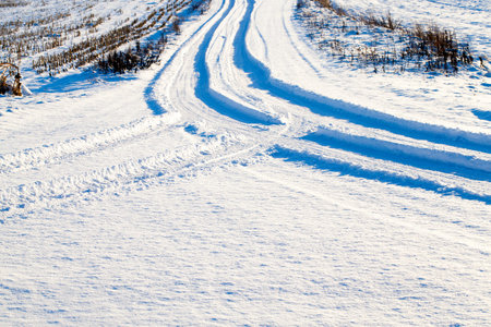 traces of wheels of the car on the snow-covered road. Photographed close-up. On the sidelines of growing grass or cut corn stalks.の写真素材