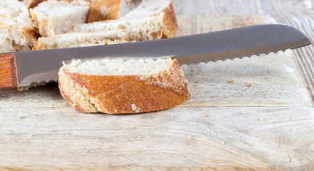 cut into pieces of baguette. photo close-up of a bread knife, inside a loaf, lying on a wooden...