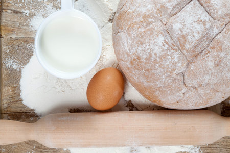 Baked rye bread, white flour, egg, milk and rolling pin lying on a wooden board and prepared for...