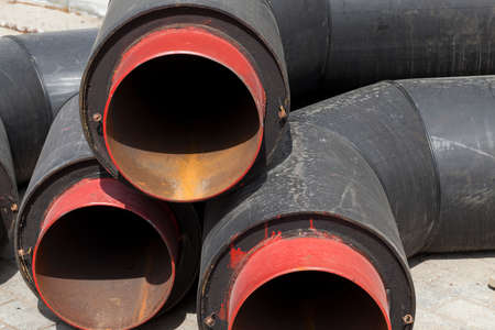 Large diameter wide metal pipes covered with a thick layer of black rubber. Close-up photo during sewer construction worksの写真素材