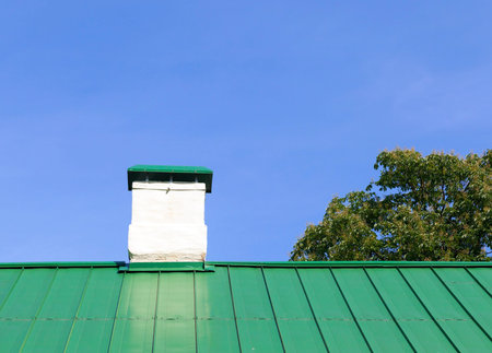 Concrete plastered chimney photographed in the summer. Green metal roof of the building. Photo close...