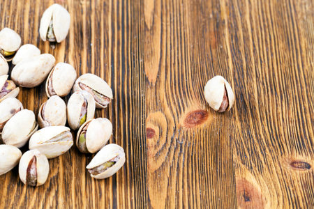 whole dried with salt pistachio nuts on a wooden surface. photo close-up on top. one nut lies...
