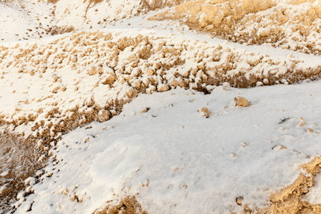 Photographed several piles of sand covered with a thin layer of snow in the field. Winter time of...