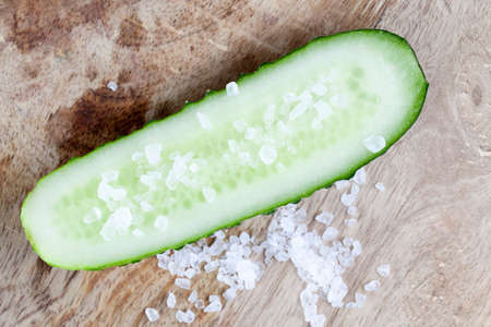 salt poured over half a cucumber of coarse grinding, a photo on a wooden backgroundの写真素材
