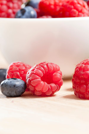 lying on a light board of raspberries and blueberries during the harvest, in the background a white...