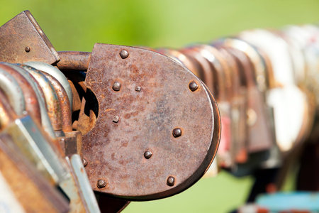 old rusty metal padlock with other locks closed on the railing of the bridge in connection with the...