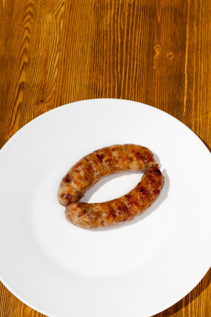two pork sausages lying on a white plate on a wooden table, top view