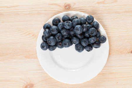 ripe blueberries lying on a white plate on a wooden table, closeupの写真素材