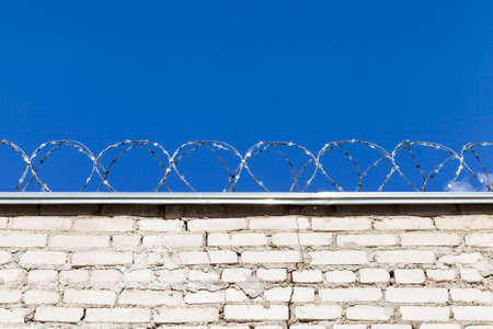 old brick fence, with a barbed old wire, private territory, against a blue sky background closeupの写真素材
