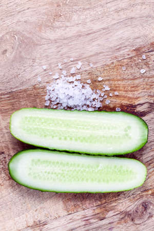 Sliced along a ripe green cucumber, salt and vegetables on a cutting board, closeupの写真素材