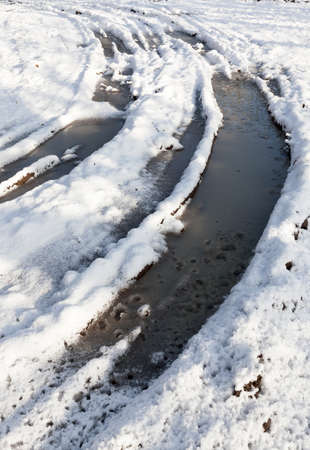 a deep rut in the mud covered with snow, part of which began to melt, a very bad road, a closeup in the forestの写真素材