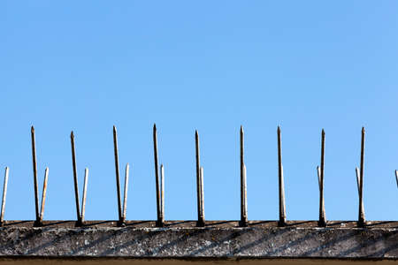 old brick fence on top of which metal spikes are installed to protect the territory, against the background of the blue sky, close-up and detailsの写真素材