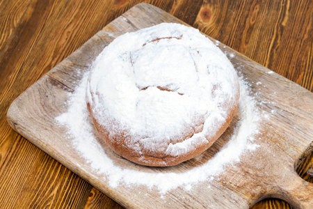 fresh round bread sprinkled with white wheat flour during its preparation, closeup on top