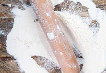 scattered on a cutting board white rye or wheat flour together with a wooden rolling pin, closeup on topの写真素材