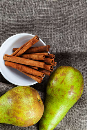 fresh harvest of green pears lying together on a linen tablecloth with whole fragrant cinnamon, closeup, top viewの写真素材